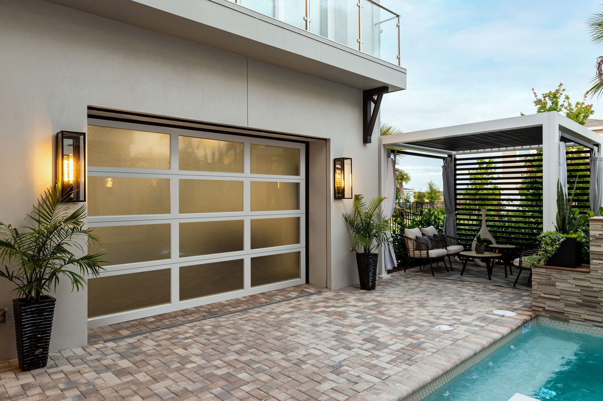 Garage door and patio area with pool; white garage door, brick patio, pergola, and plants.