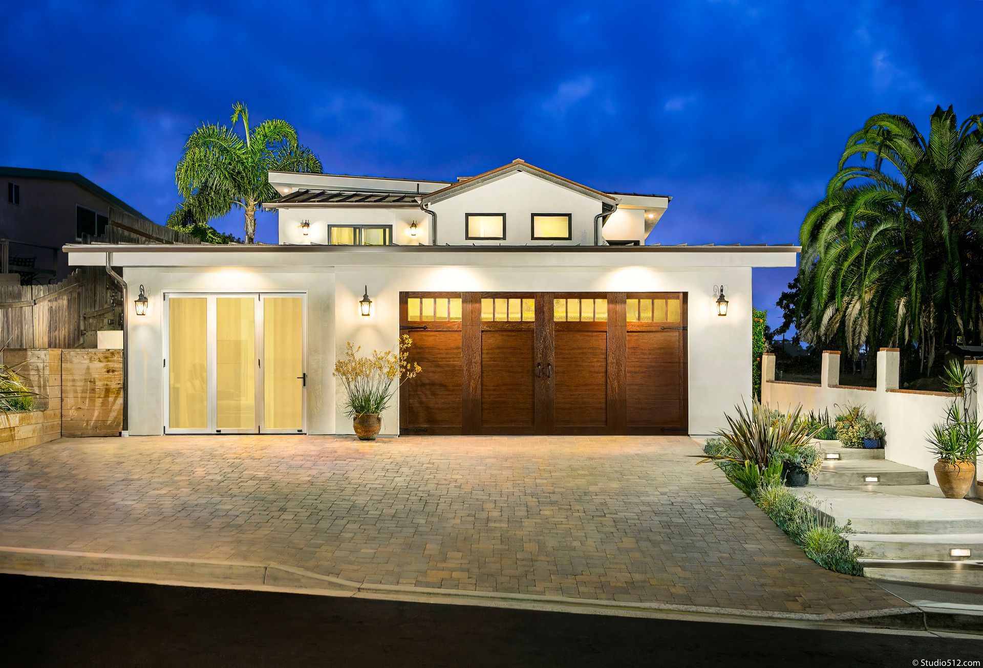 White house with dark brown garage doors and a stone driveway at dusk.