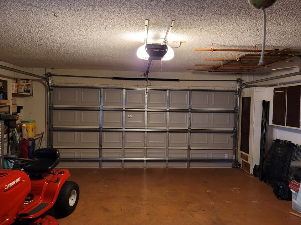 A garage with a lawn mower and a garage door open.
