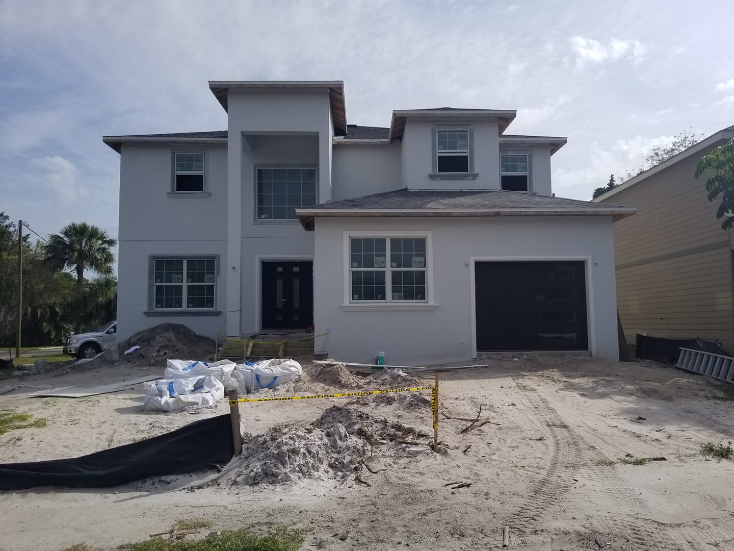 A large white house with a black garage door is under construction.