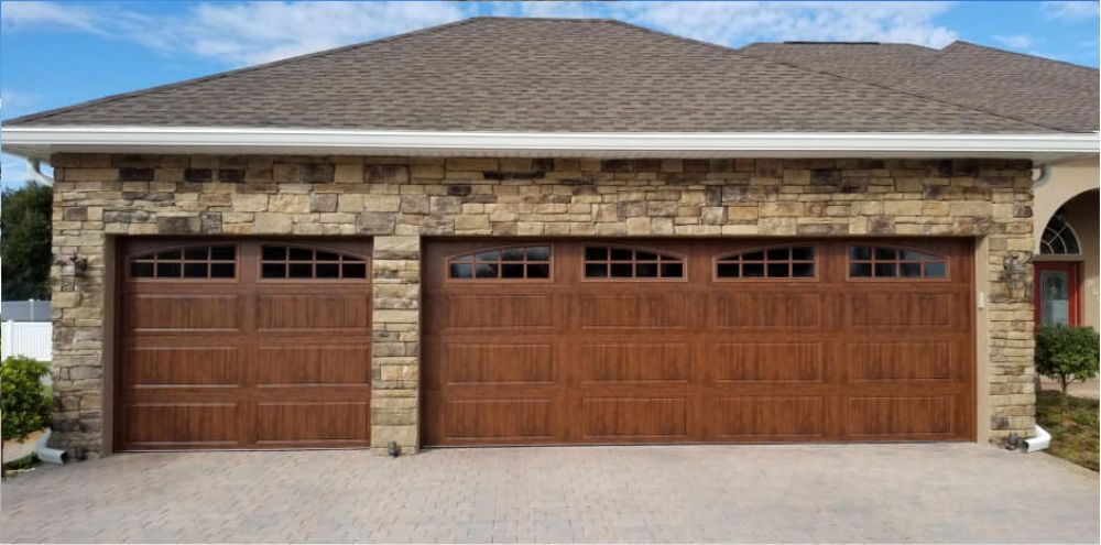 A large house with a wooden garage door and a stone wall.