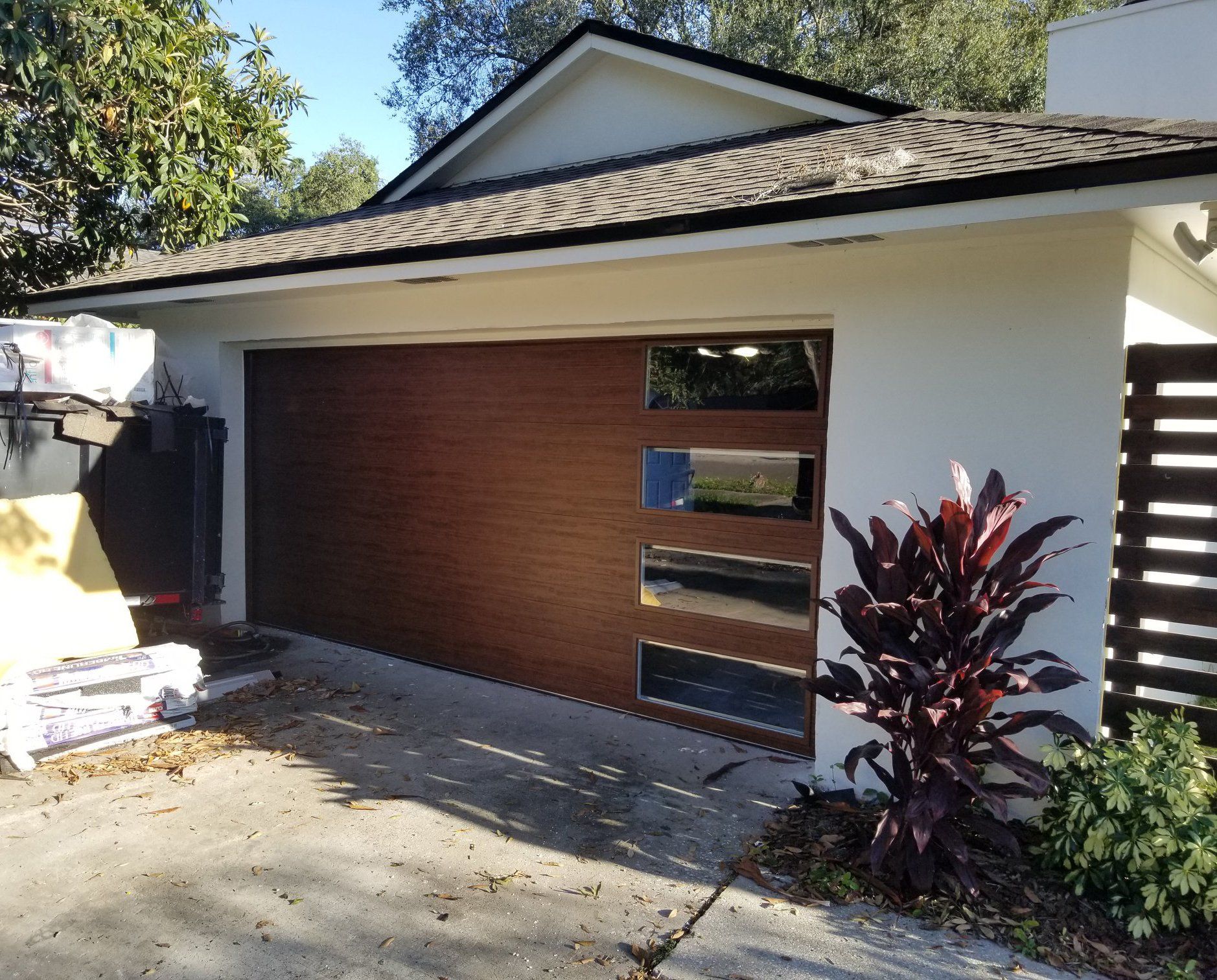 A white house with a wooden garage door and a plant in front of it.