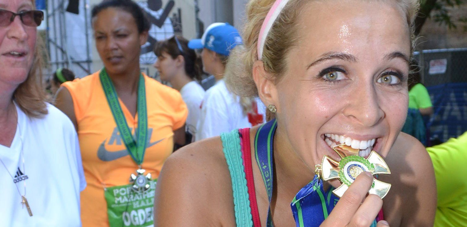 A woman is holding a medal in her hand and smiling.