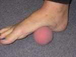 Foot rolling a pink ball on a gray carpet, for foot massage or physical therapy.