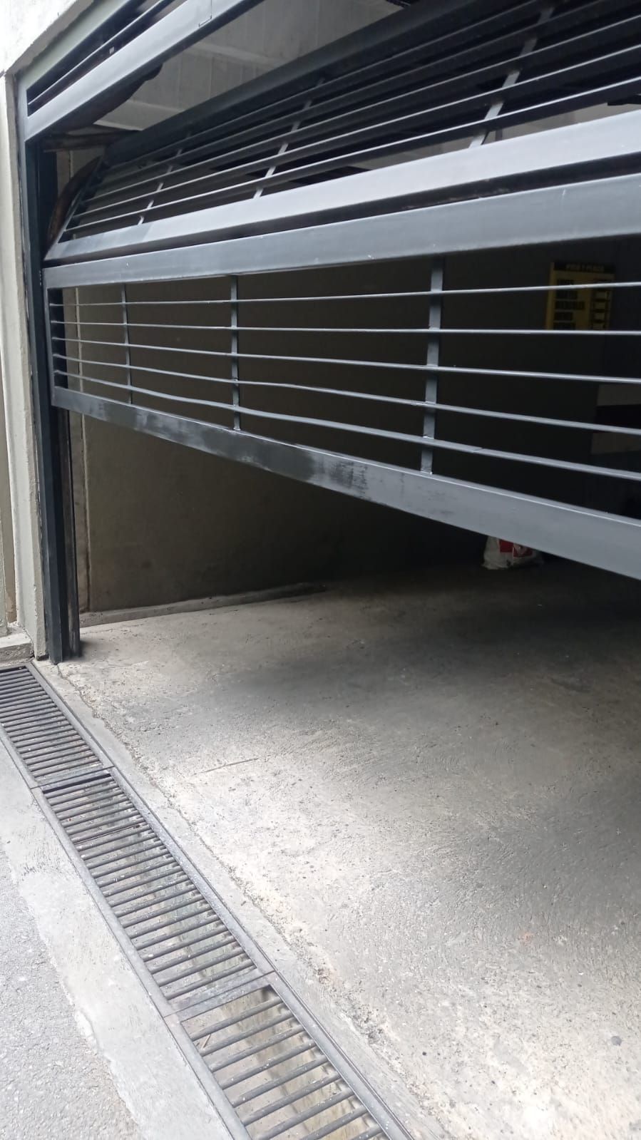 Tres personas trabajan en la fachada de una tienda con una persiana de seguridad de metal negro, mientras que otra sube por una escalera dentro del local.