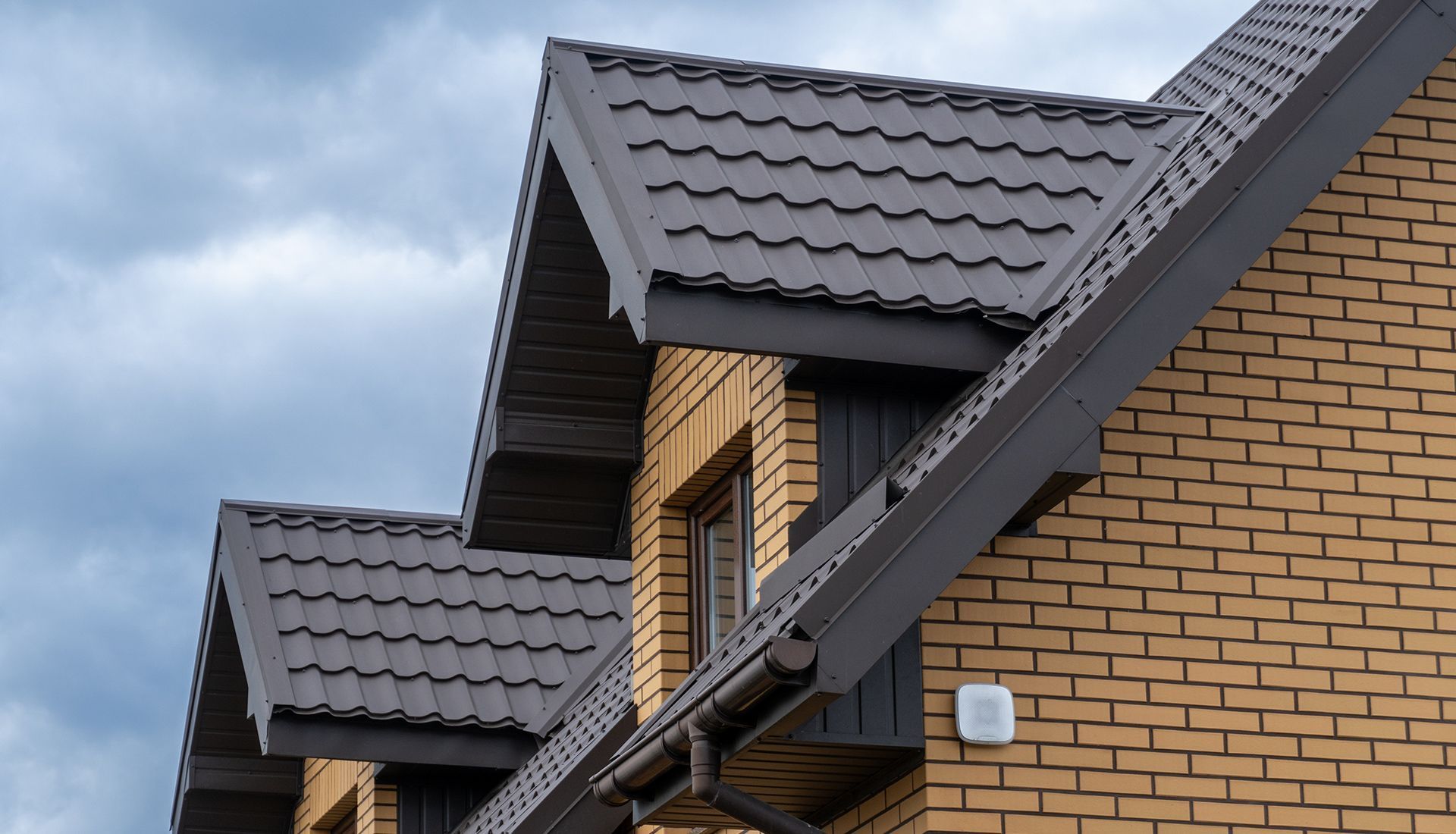 Brick building with brown metal roof against a cloudy sky.