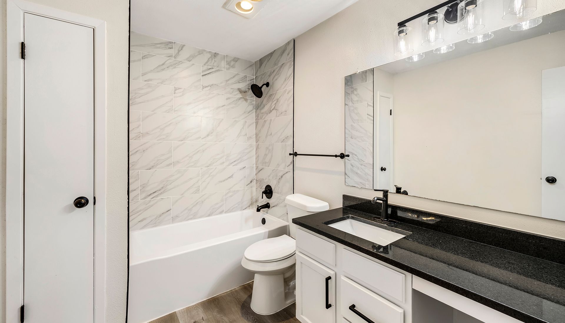Bathroom with white marble-like tile in shower, black fixtures, white vanity with black countertop, and a large mirror.