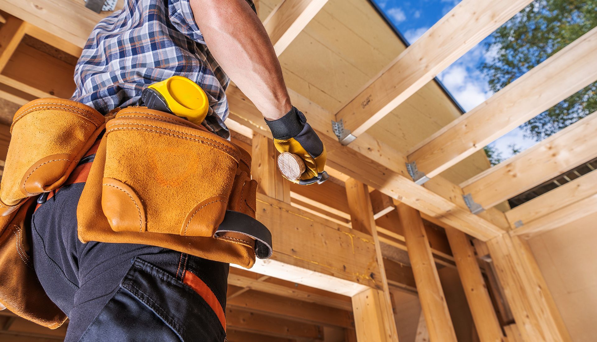 Carpenter wearing a tool belt, working on a wooden frame structure.