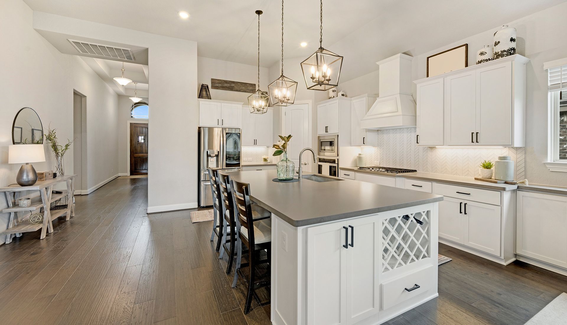 Spacious white kitchen with dark gray island, stainless steel appliances, and dark hardwood floors.