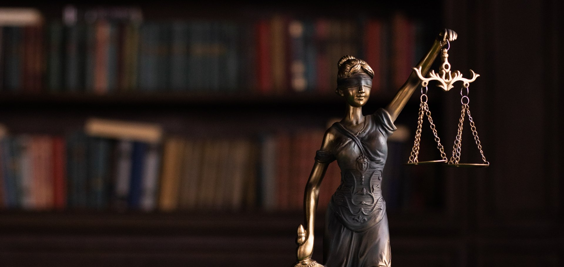 Bronze statue of Lady Justice holding scales, symbolising fairness and impartiality, with a blurred 