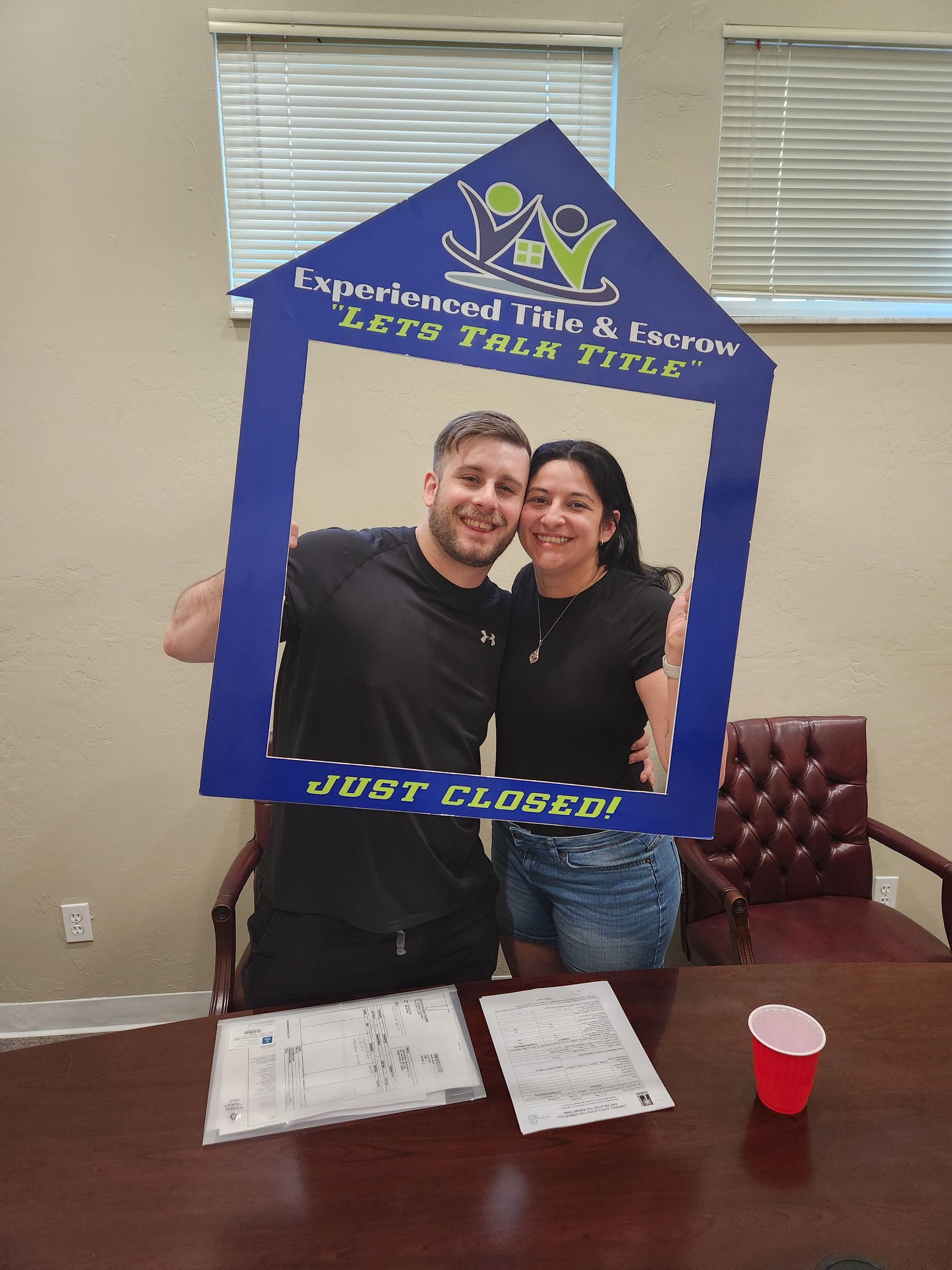 A man and a woman are posing for a picture with a picture frame in the shape of a house.