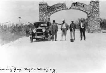 A group of men are standing next to a car in front of a stone archway.
