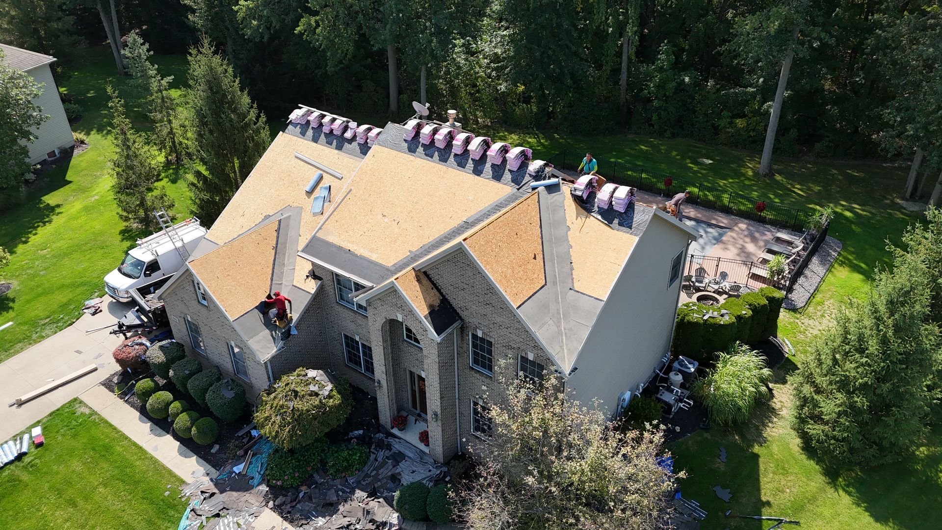 Roof replacement in progress with exposed decking and crew installing shingles on residential home
