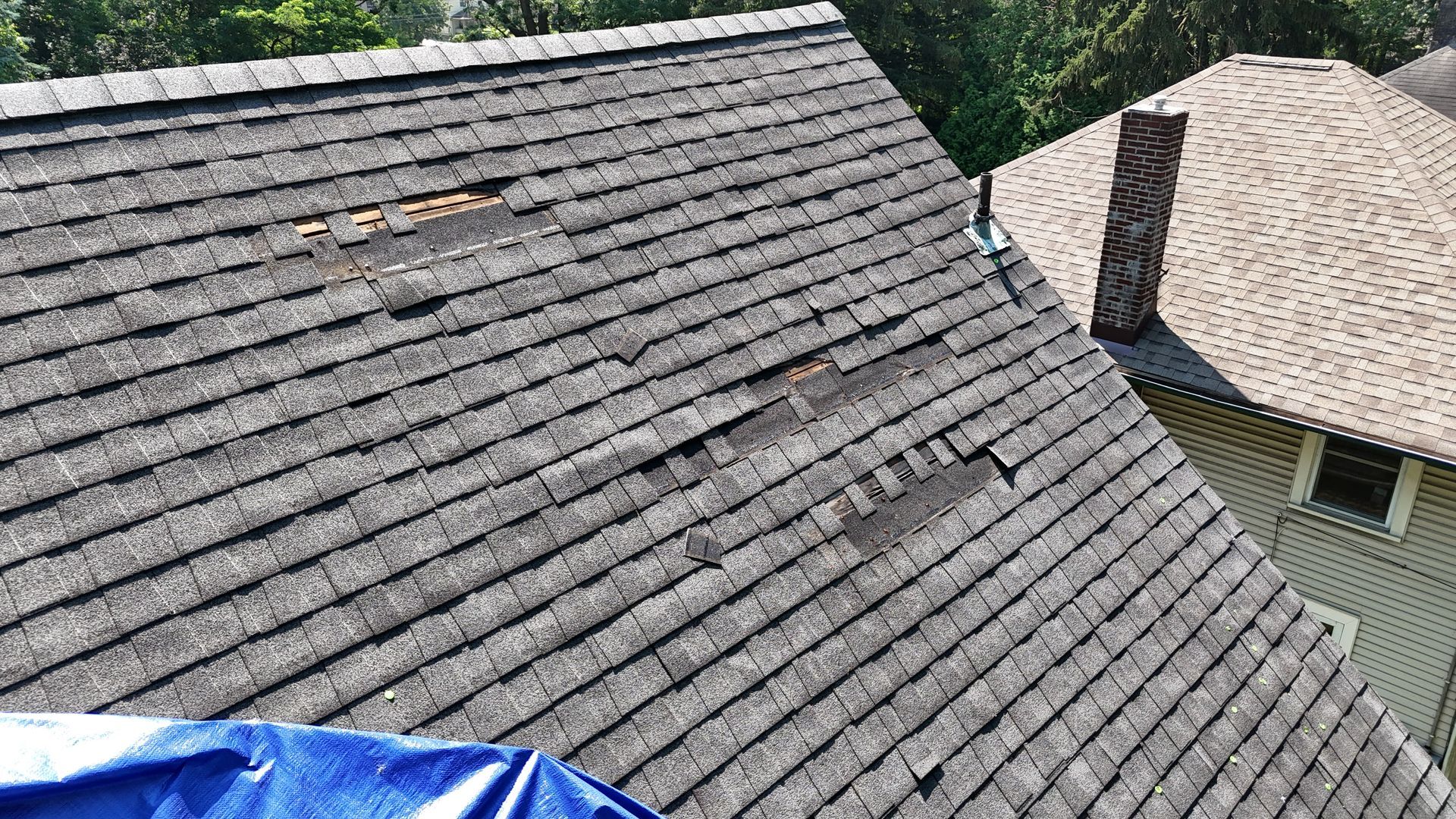 Missing and damaged shingles on roof from storm damage showing exposed underlayment and wear
