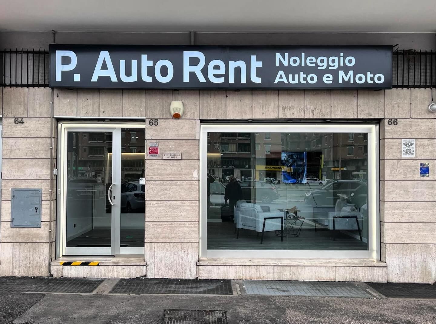 Vetrina del negozio P. Auto Rent con insegna illuminata; offre noleggio di auto e moto.