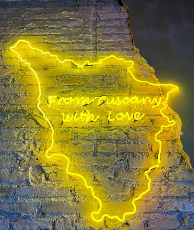 Insegna al neon gialla: contorno della Toscana con la scritta 