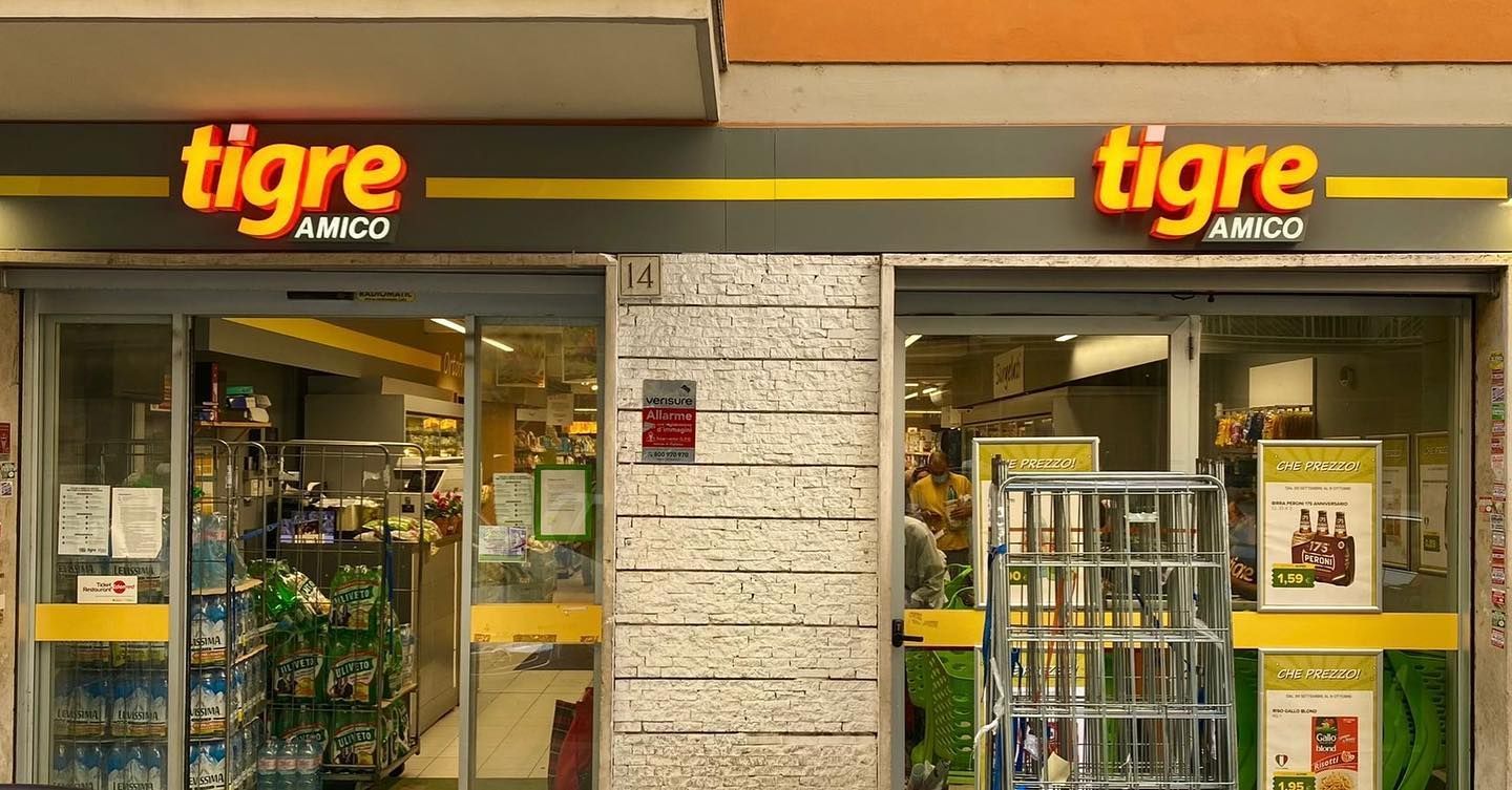Facciata del negozio Tigre Amico con insegne arancioni e gialle, porte in vetro e prodotti visibili all'interno.