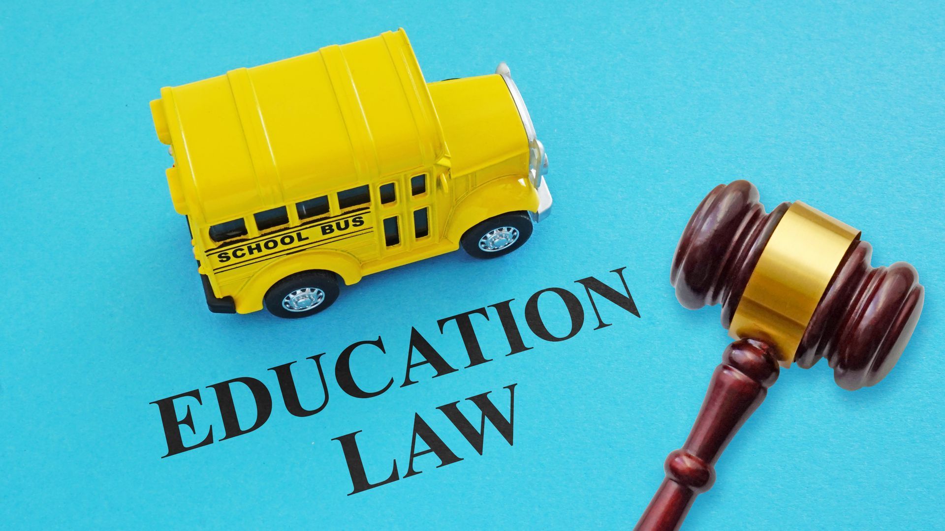 Toy school bus and wooden gavel placed on a blue surface with the words ‘Education Law.’