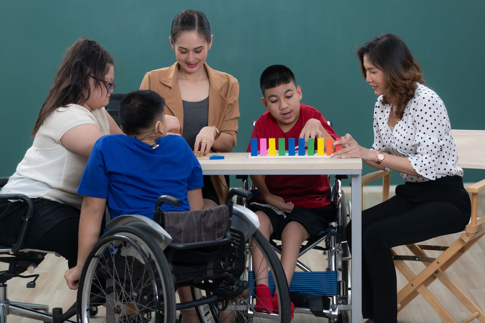 A group of special kids and adults at a table playing with colorful domino blocks in a classroom