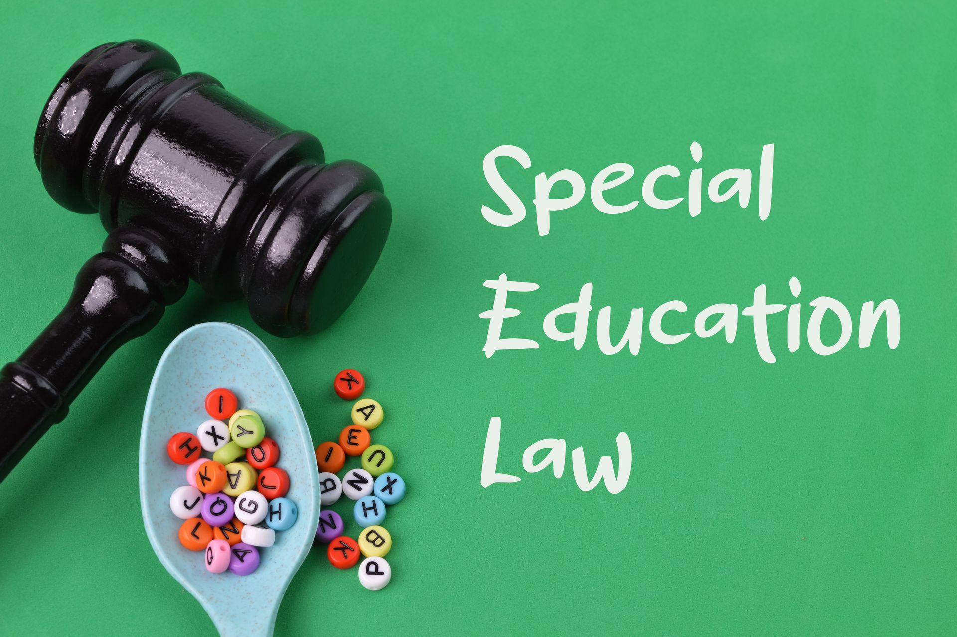 Gavel beside a spoon of colorful alphabet beads on a green surface labeled ‘Special Education Law.’