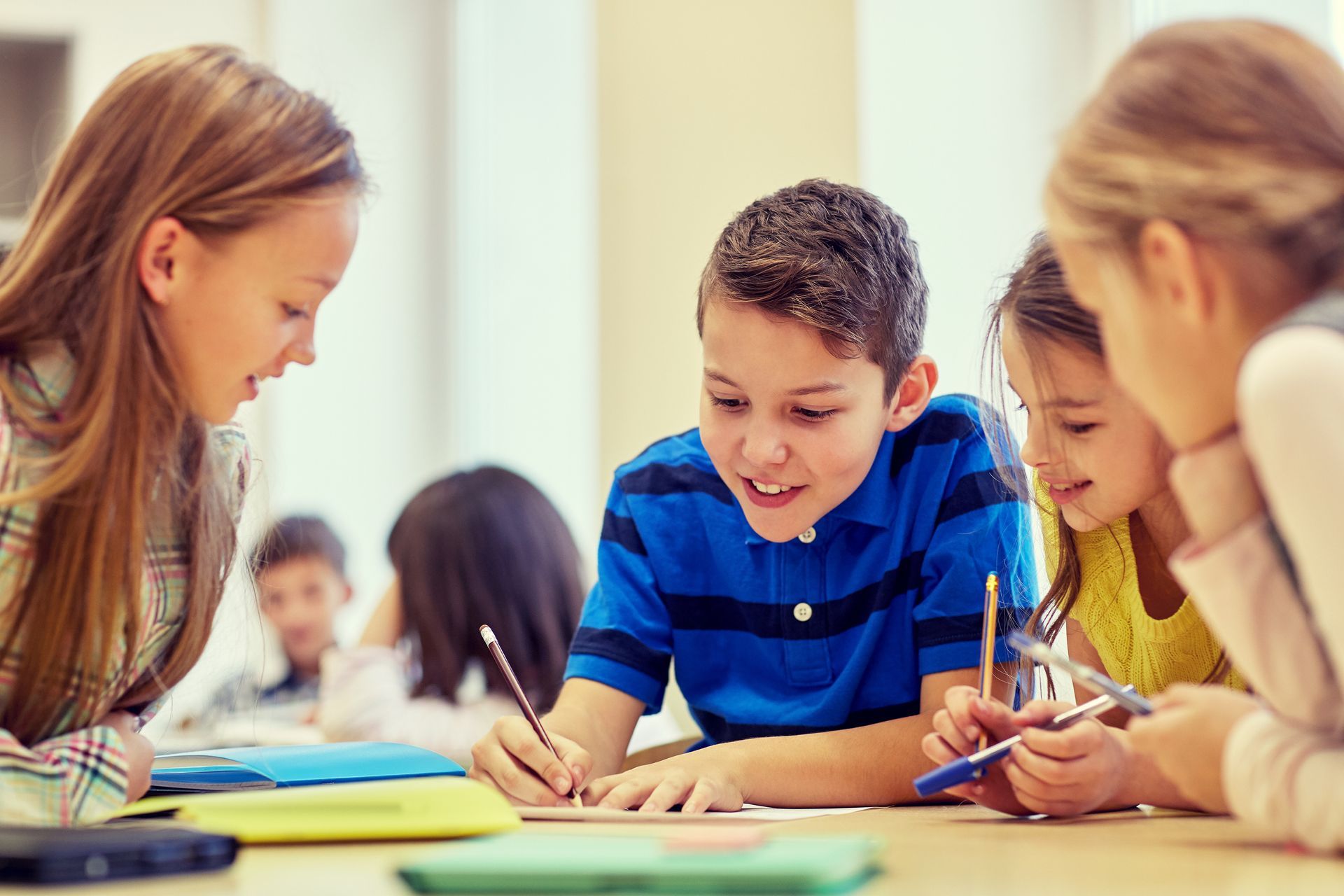 Students working together at a table, writing in notebooks, and collaborating on a classroom activity.