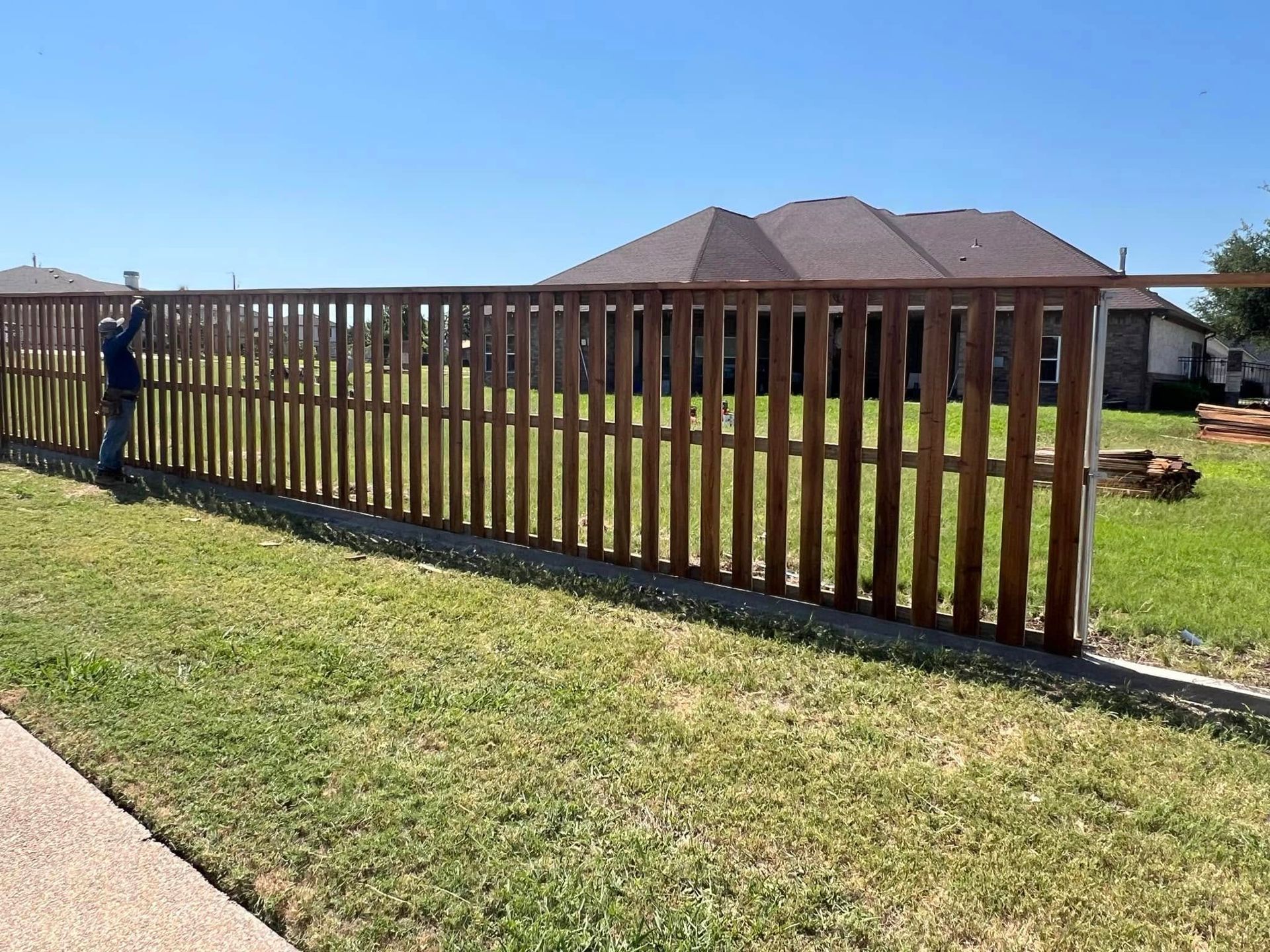 A man is standing next to a wooden fence in front of a house.