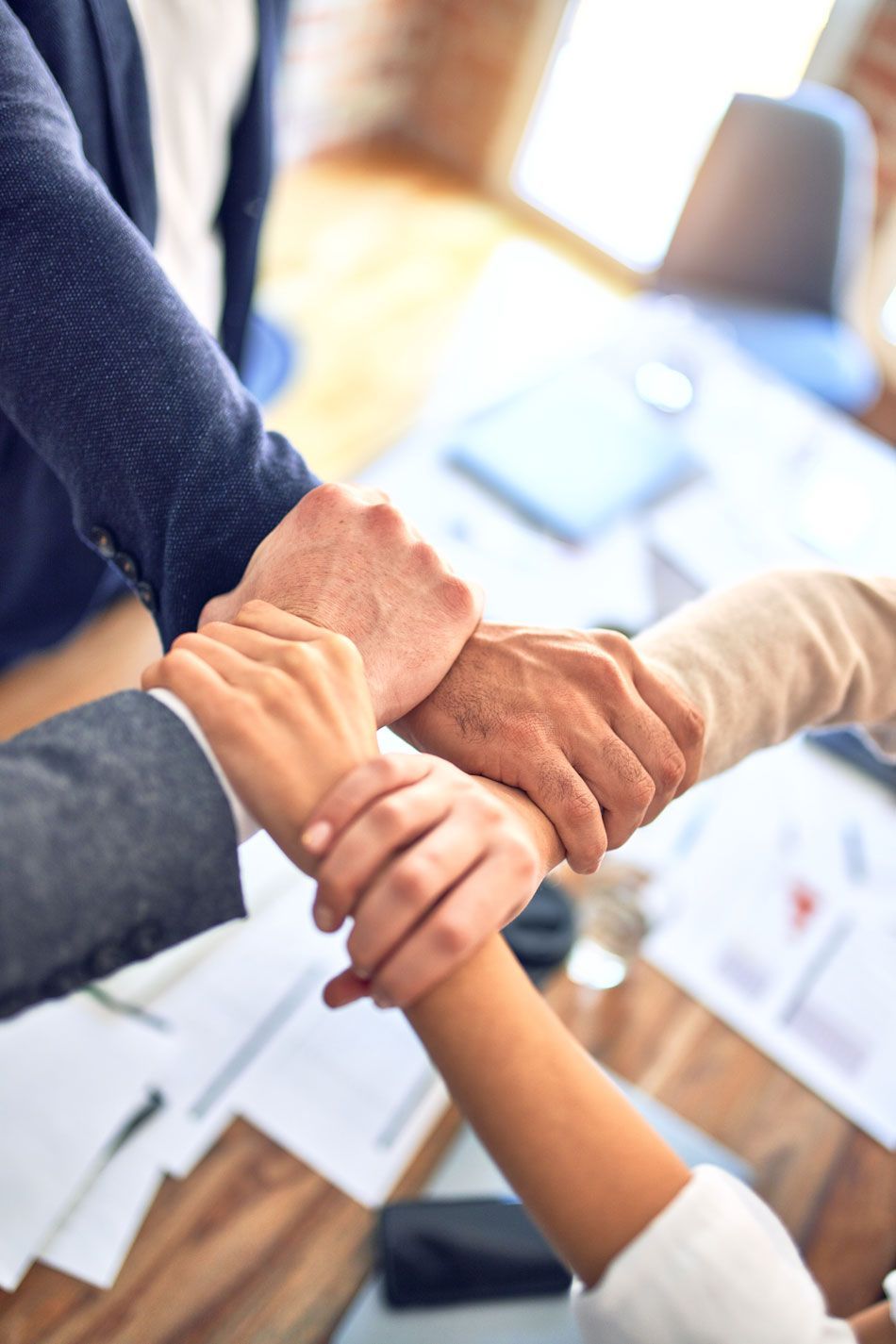 People in business attire clasping wrists together at a table, symbolizing teamwork.