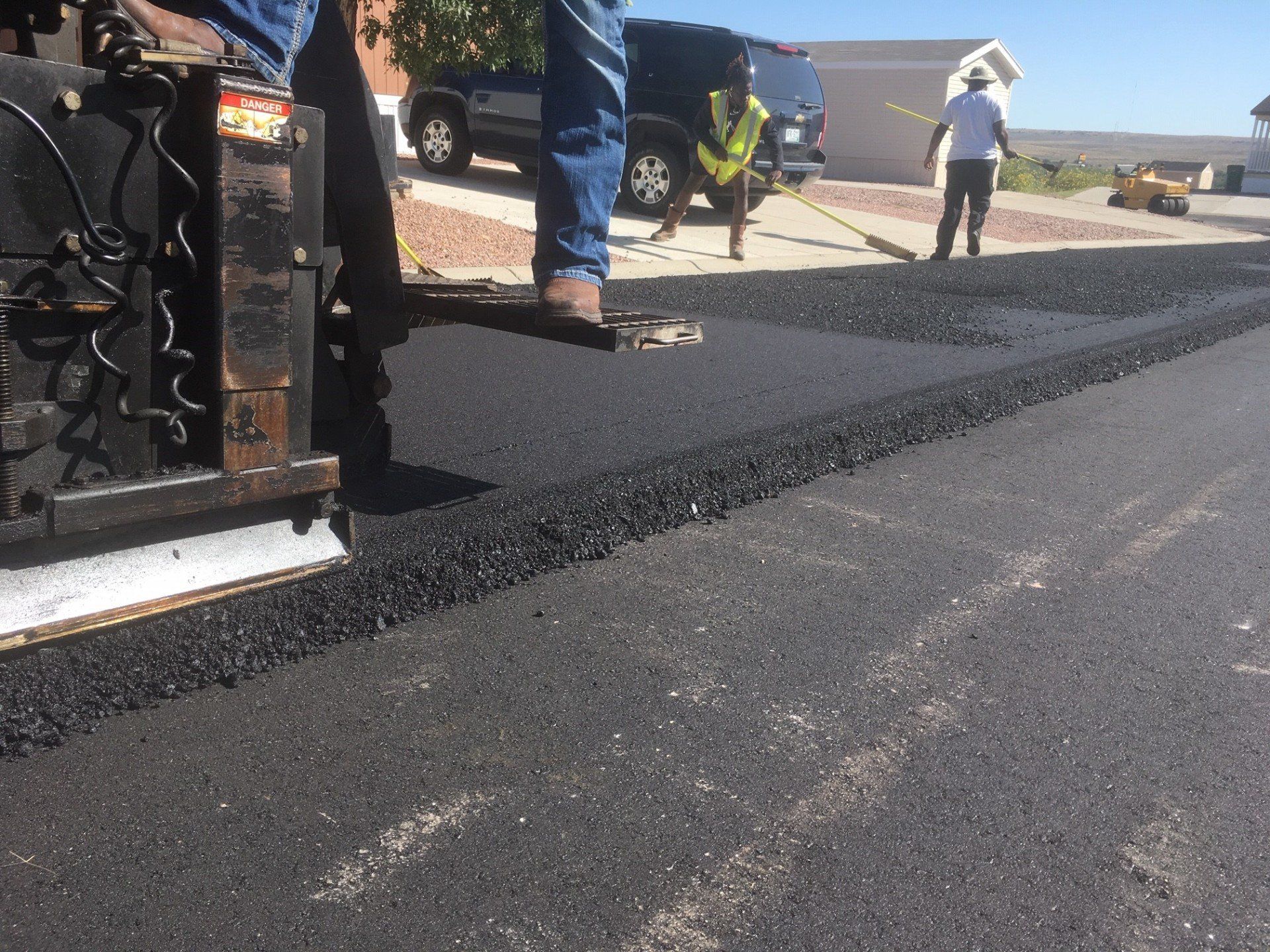 A man is standing next to a machine that is laying asphalt on a road.