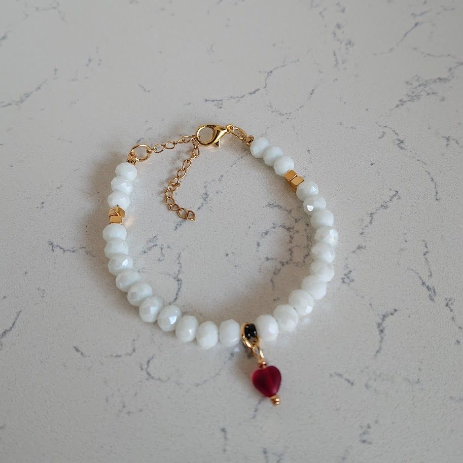 armband van witte facetkralen met een rode hartjesbedel en dq gouden tussenkralen en sluiting met verlengkettinkje