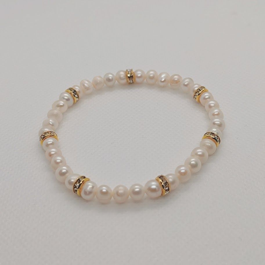 Armband met witte zoetwaterparels met ss gouden tussenkralen met zirkonia geregen op elastiek gedragen om een pols.