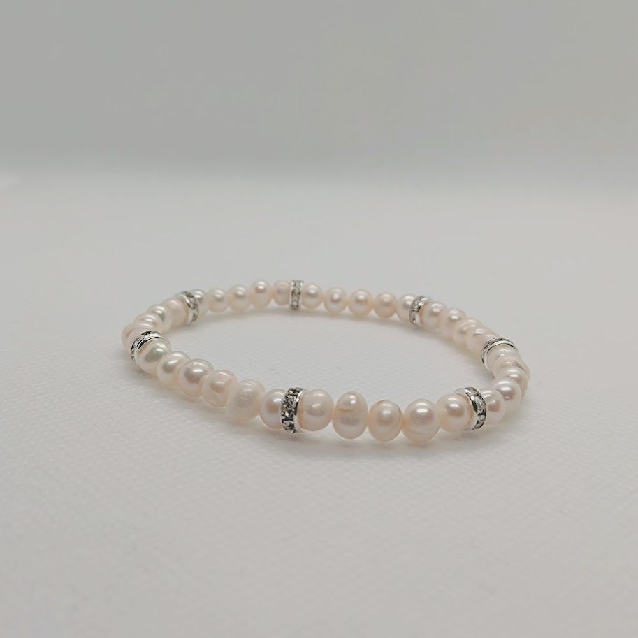 Armband met witte zoetwaterparels met stainless steel gouden tussenkralen met zirkonia geregen op elastiek.