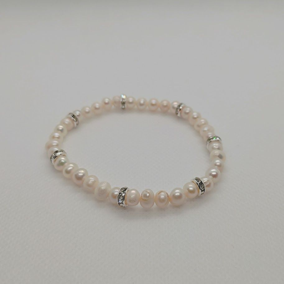 Armband met witte zoetwaterparels met ss zilveren tussenkralen met zirkonia geregen op elastiek gedragen om een pols.
