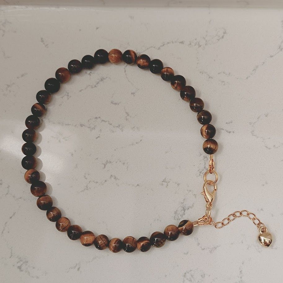 Enkelbandje van tijgeroogkralen met een hartjesbedel aan het verlengkettinkje.