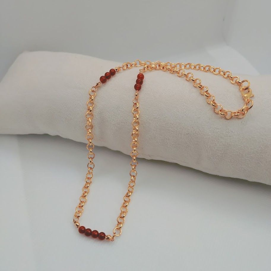 Stainless steel schakelketting met kleine carneool tussenkralen liggend op een kussentje