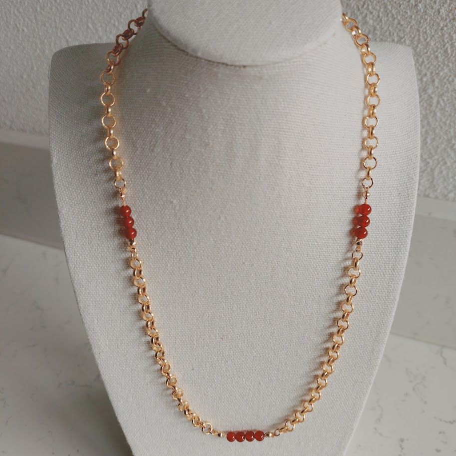 Stainless steel schakelketting met kleine carneool tussenkralen liggend op een kussentje