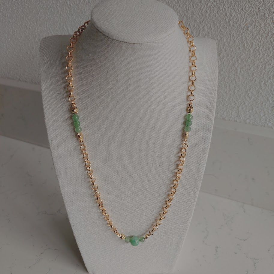 Stainless steel schakelketting met kleine groene aventurijn tussenkralen liggend op een kussentje