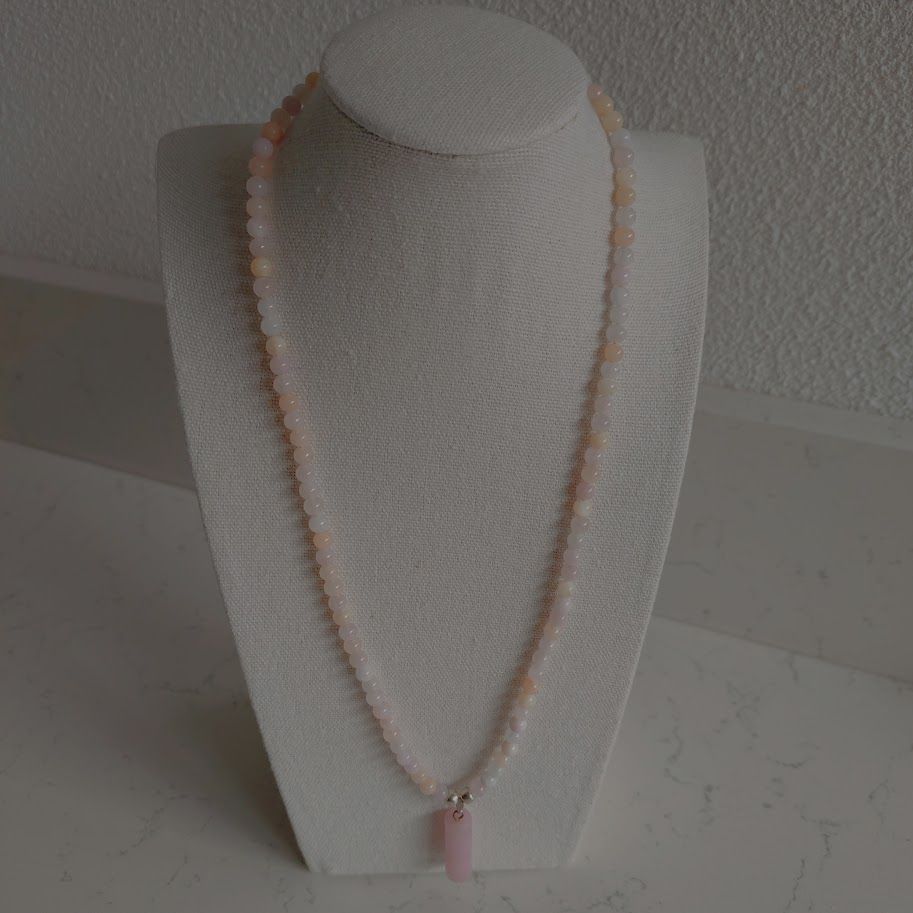 Ketting van kralen van pastel jade met een rozenkwarts hanger liggend op een kussentje.