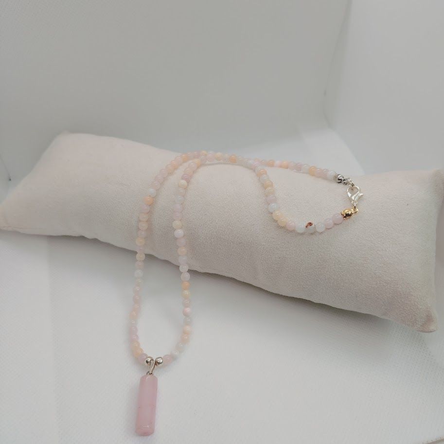 Ketting van kralen van pastel jade met een rozenkwarts hanger liggend op een kussentje.
