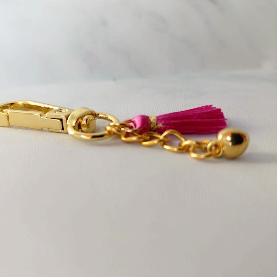 Sleutelhanger van stainless steel gold met een hartjesbedel aan een schakelkettinkje en een roze kwastje.