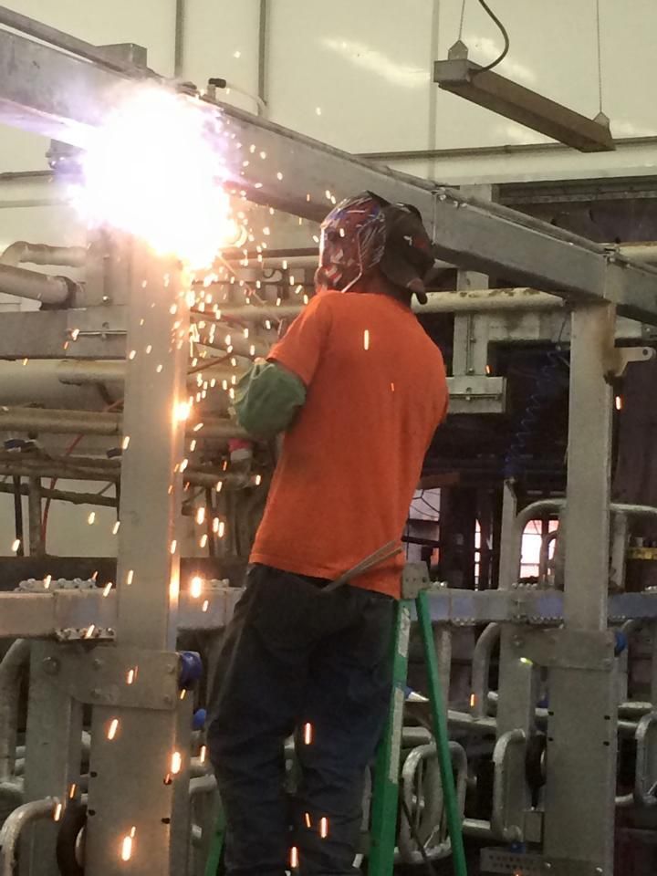 A man in an orange shirt is welding a metal structure