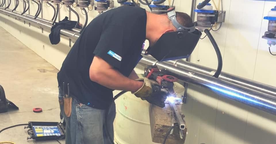 A man is welding a pipe in a factory.