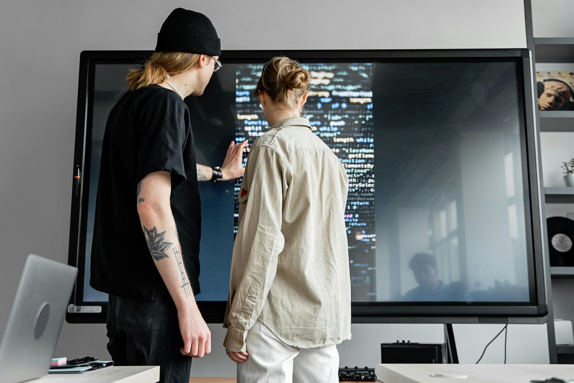 Two people looking at a large screen displaying lines of code. One points at the screen.