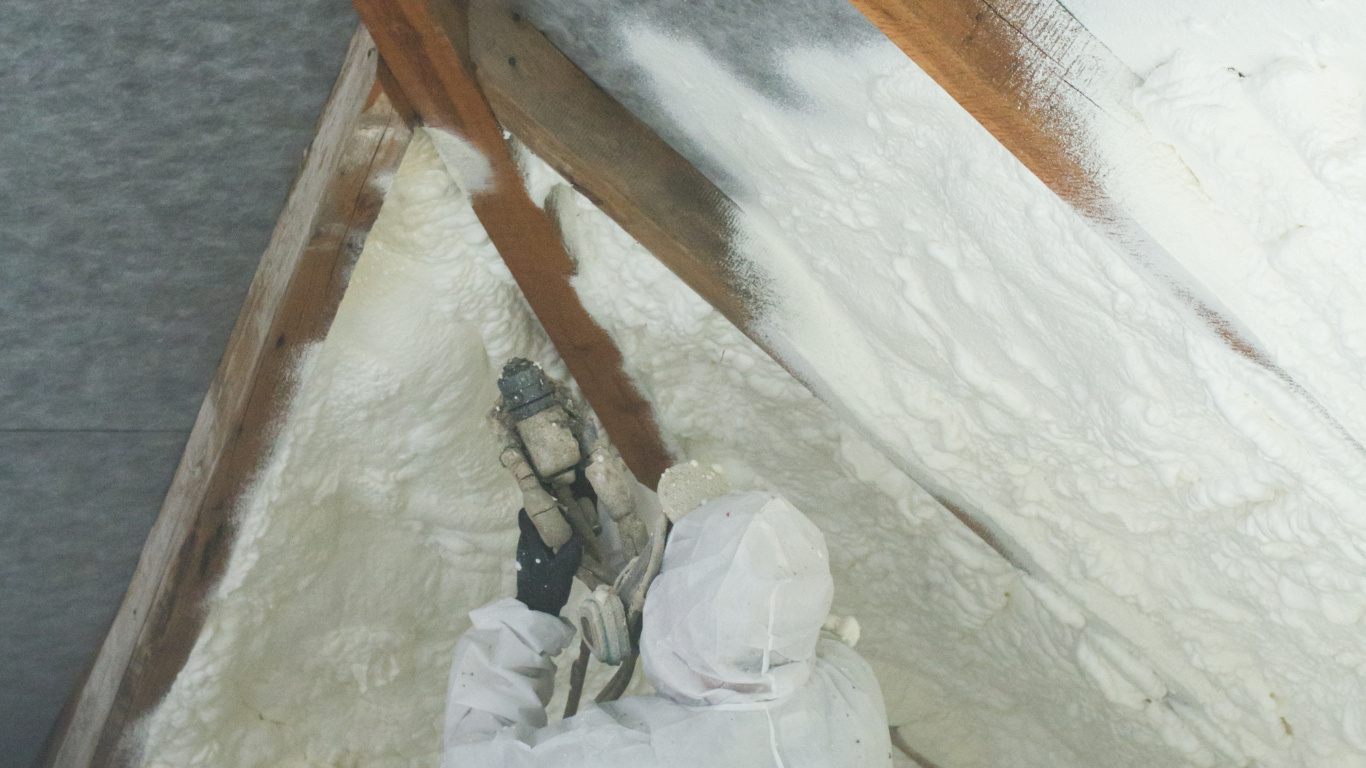 Technician spraying spray foam insulation into an attic corner, fully equipped with protective mask and gear for safe, efficient, and airtight insulation in County Limerick.