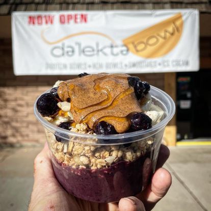 A person is holding a bowl of food in front of a sign that says now open