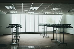 Empty room with several clothing racks in front of a large window. Beige carpet, bright ceiling lights, and gray hangers.