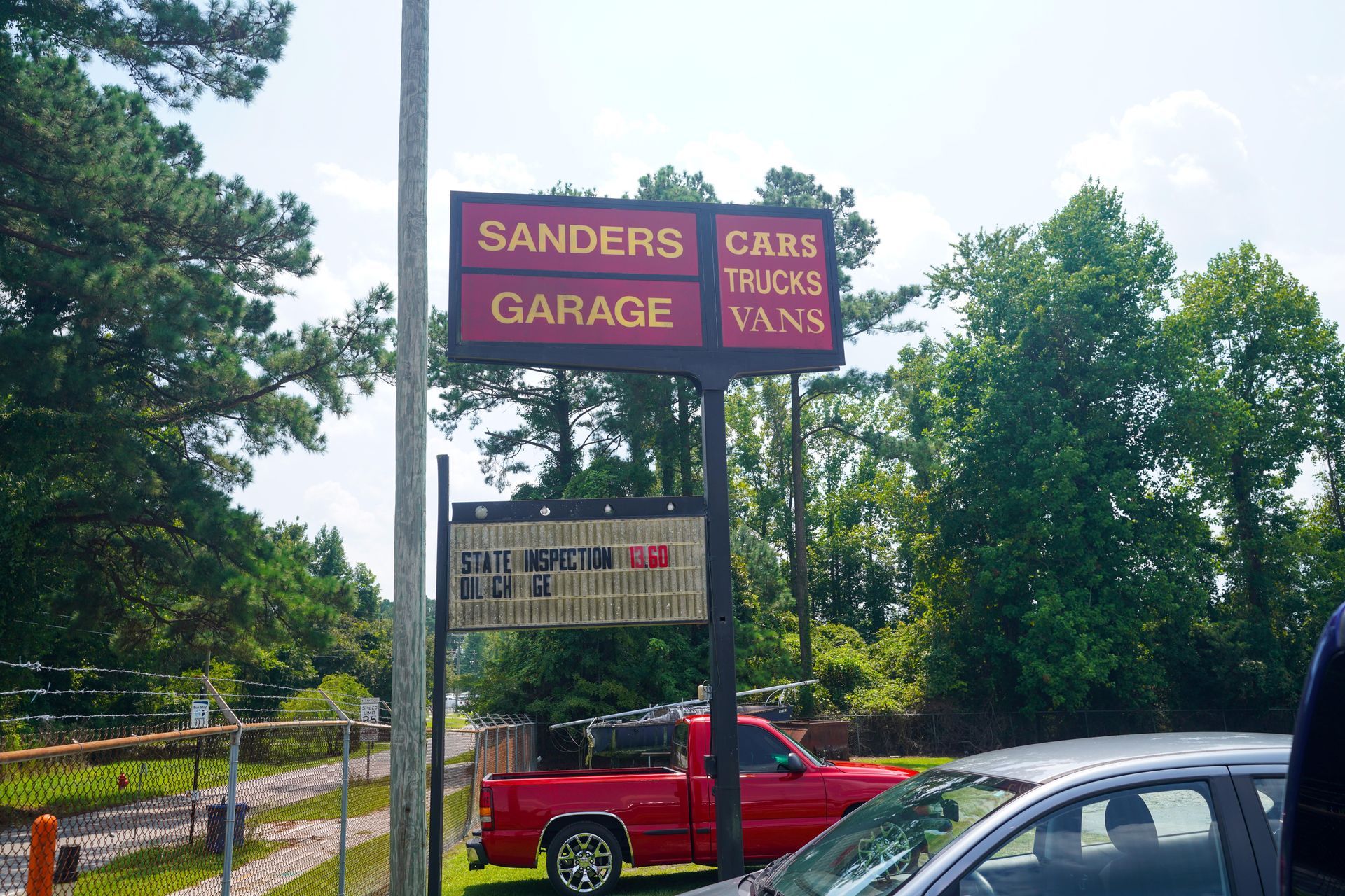 A roadside sign for Sanders Garage advertising cars, trucks, and vans, with a red truck parked behind it.
