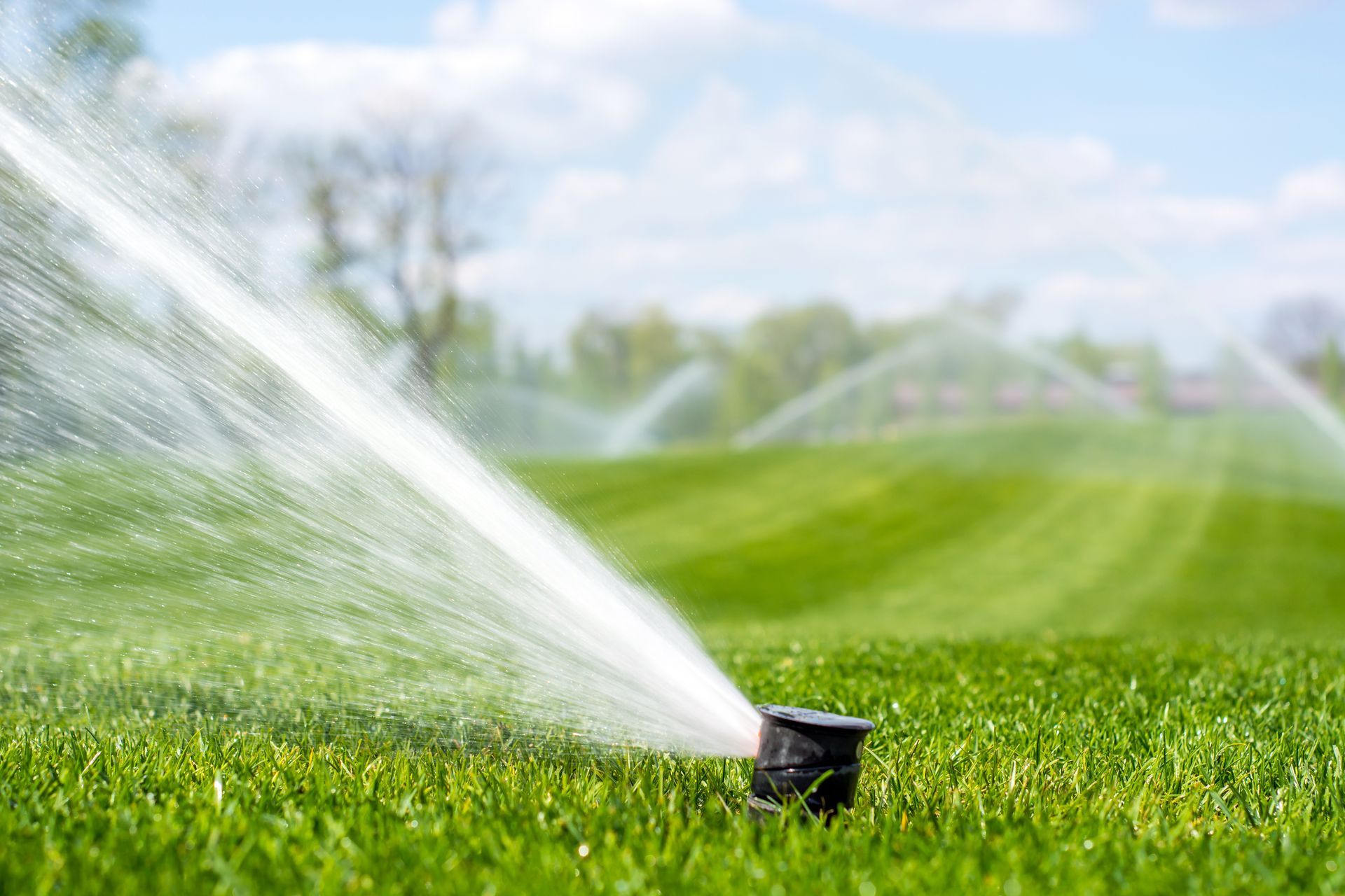 Lawn sprinkler spraying water over a green field on a sunny day