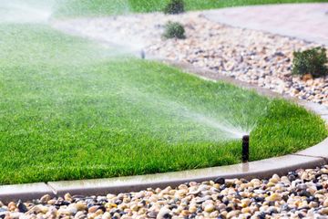 Sprinklers watering a green lawn beside a curved gravel path