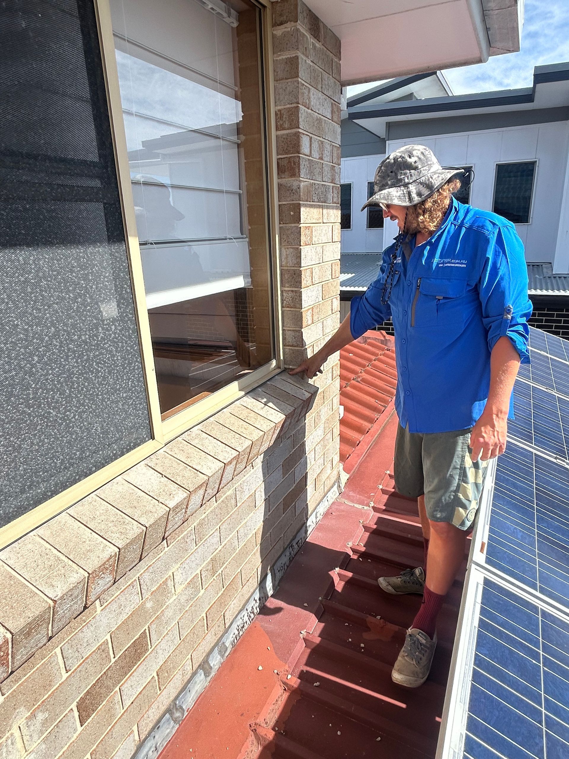 Man in blue shirt inspecting a red rooftop walkway beside a brick house