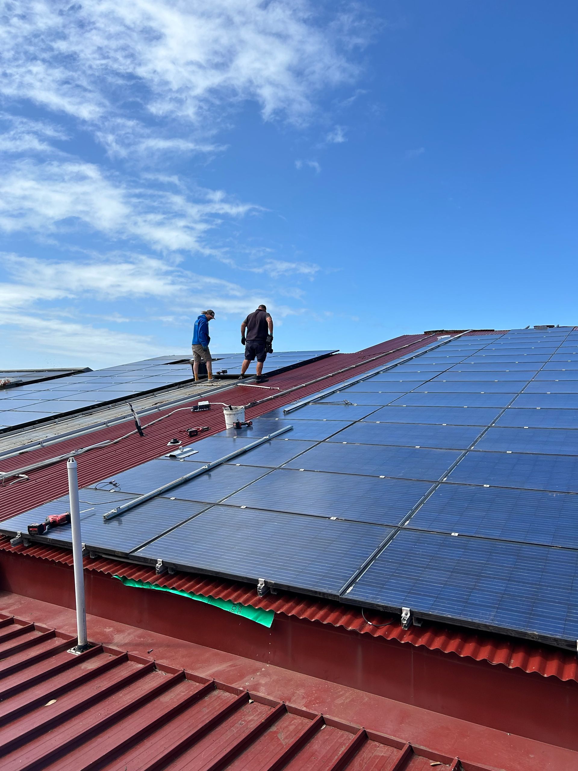 Two workers walking on a rooftop with rows of solar panels under a blue sky